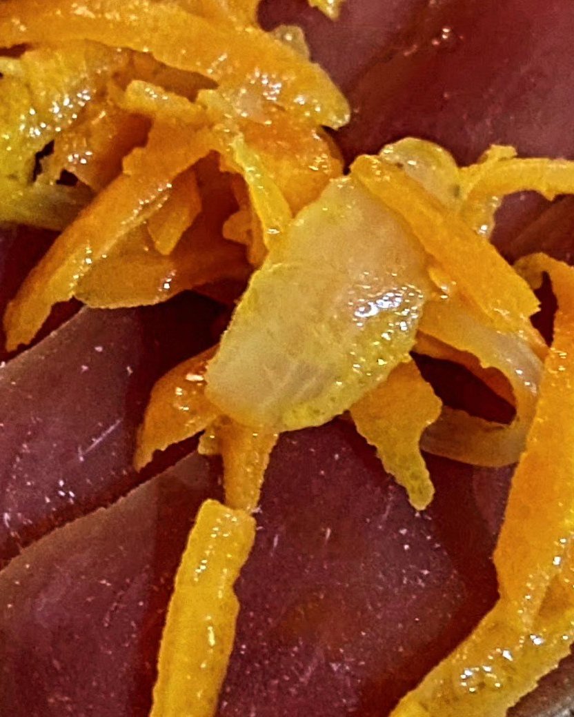 Fatias finas de muxama de atum, cor de vinho, cobertas com tiras de laranja confitada